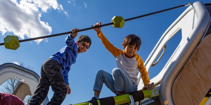 Looking up at two boys playing on a hedra structure -- they are holding onto a black cable. 