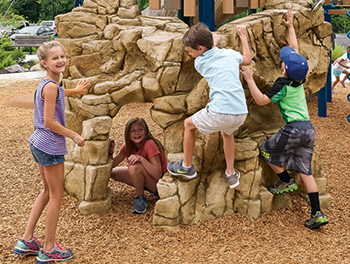 Children climb on concrete realistic playground rock formation