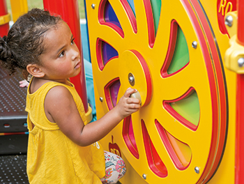 young girl in yellow dress touching color wheel panel on playground