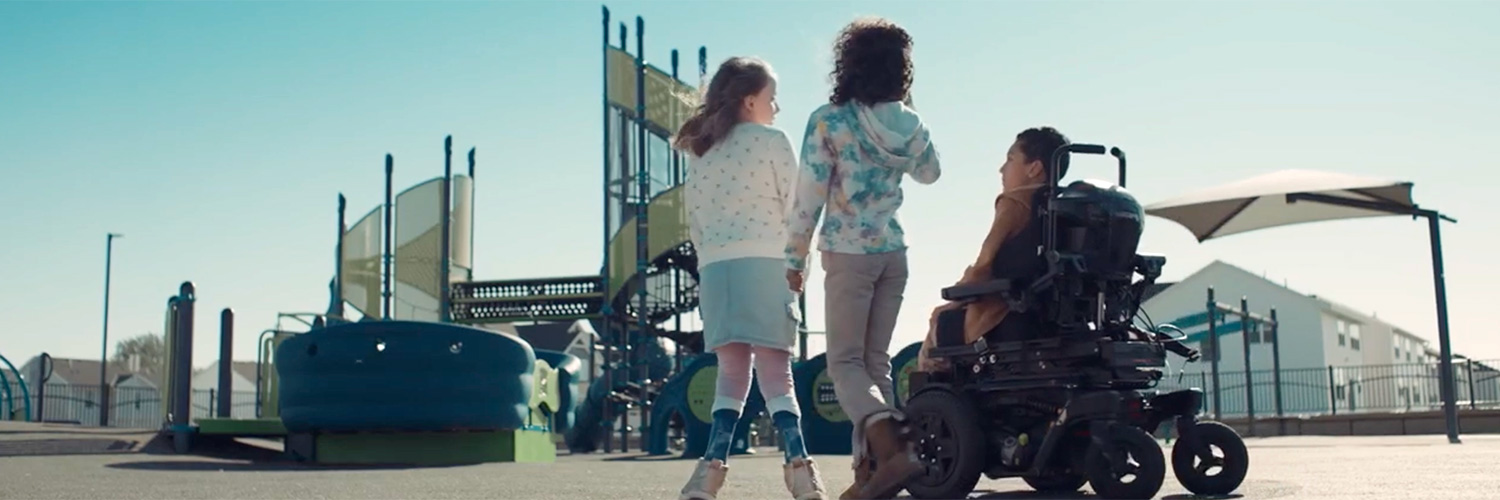 Still image from Inclusion Makes the Playground video of three children in front of a playground