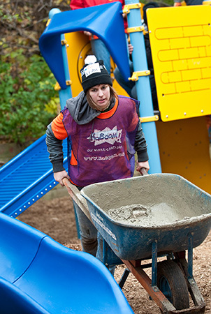 A woman pushes a wheelbarrow carrying wet cement. 