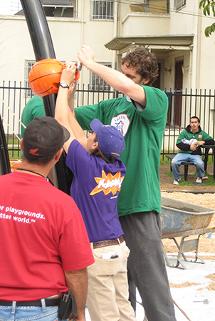 A man and a woman work on installing a playstructure while another man looks on. 