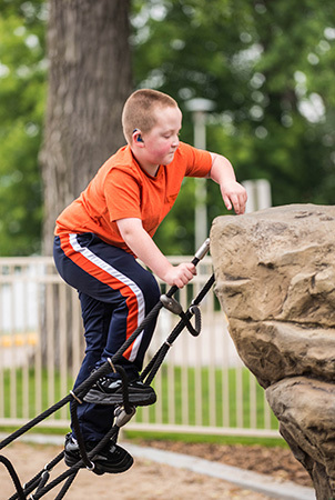 A boy climbs up a net structure leading to a rock climber. 